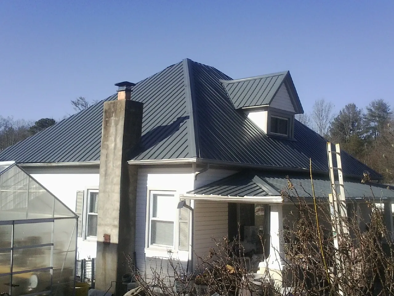Dark blue standing seam metal roof on a white farmhouse with dormer — Slate & Tile Roof Repair by Roofing Brothers in Saint Stephens Church