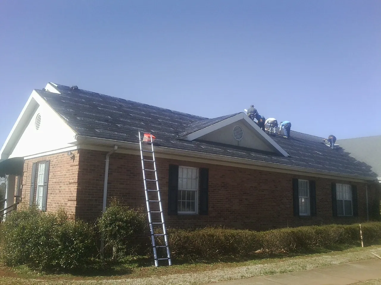 Crew tearing shingles off a brick ranch roof with a ladder set — Emergency Roof Repair work by our crew in Saint Stephens Church