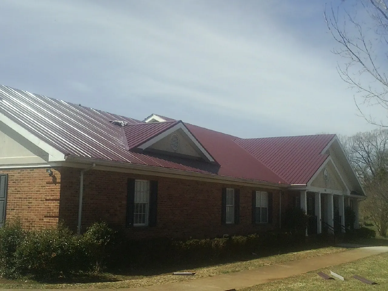 Red metal roof with gabled entries on a long brick building, from a Hail Damage Roof Repair job in Saint Stephens Church
