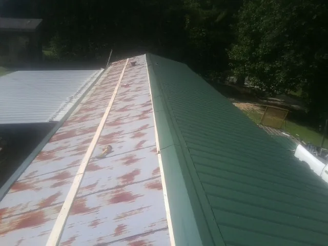 Old rusted panels beside newly installed green metal roofing — Wind Damage Roof Repair by Roofing Brothers in Saint Stephens Church