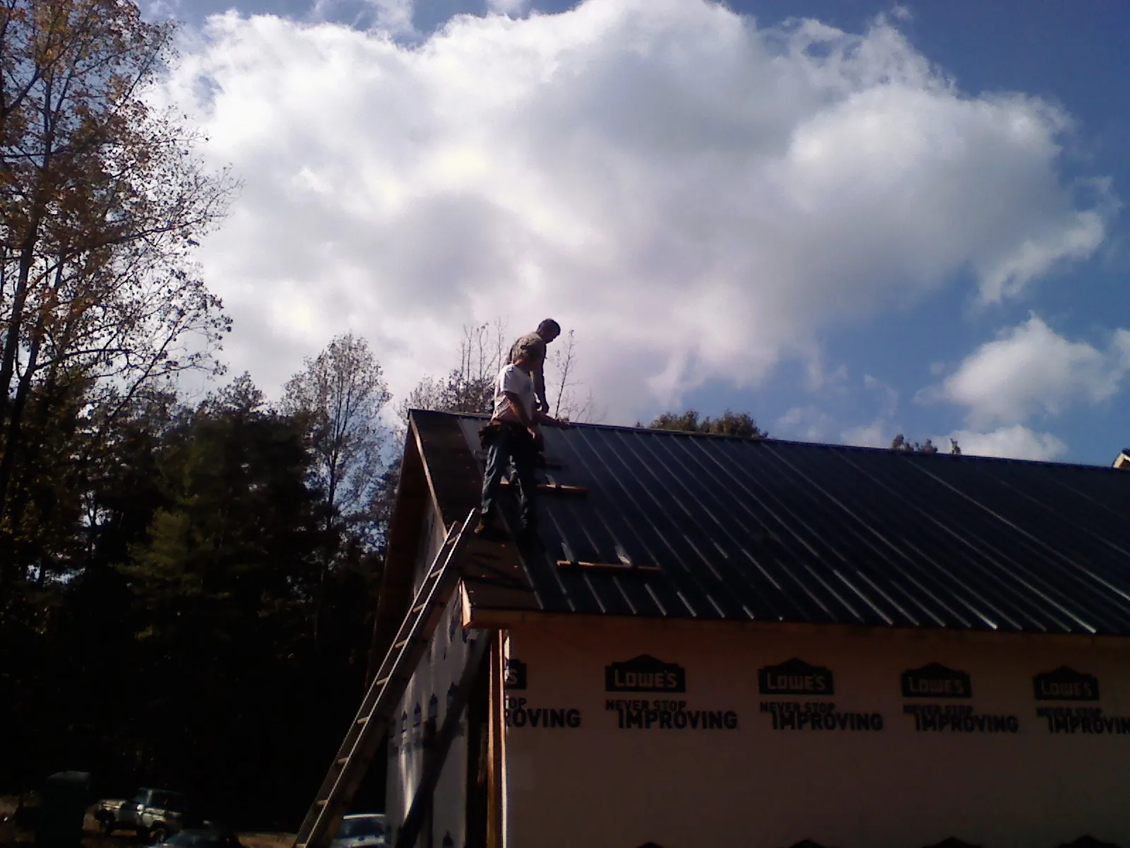 Roofer fastening dark metal panels high against a cloudy sky, from a Roof Inspection job in Saint Stephens Church