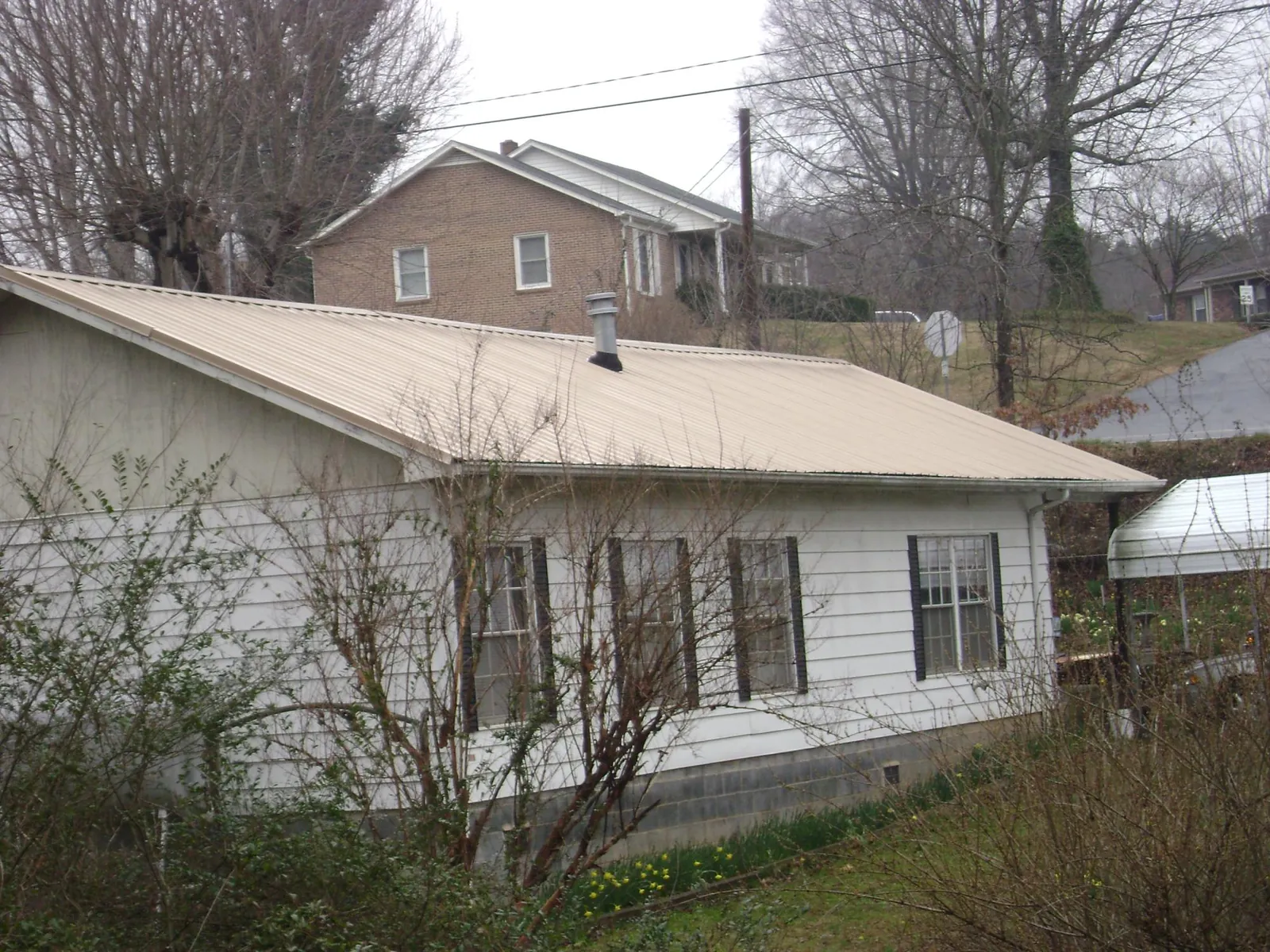 Tan metal roof on a white sided house set into a hillside — Commercial Roofing by Roofing Brothers in Saint Stephens Church