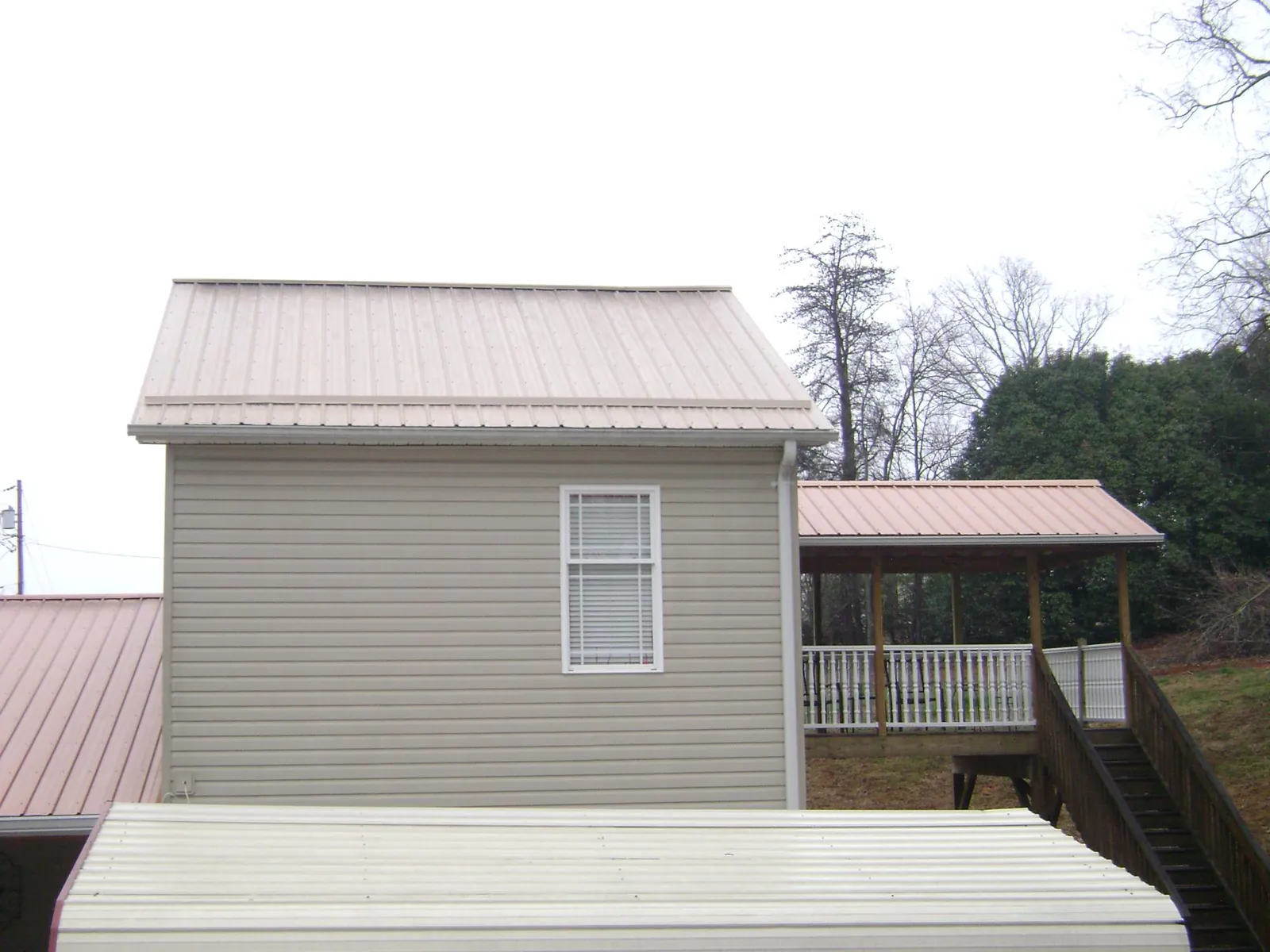 Tan metal roofs on a two story addition and attached porch, from a Roof Replacement job in Saint Stephens Church